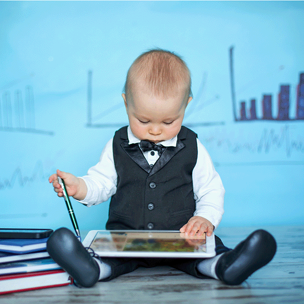 Sitting baby boy dressed in vest and bow tie holding an ipad
