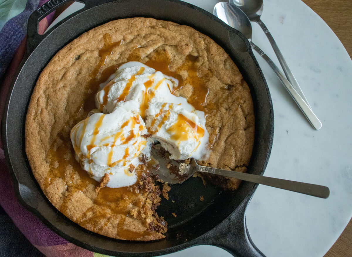 A warm skillet cookie topped with vanilla ice cream and a drizzle of caramel sauce.