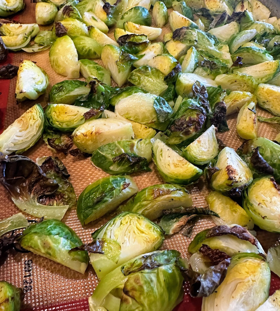 Roasted brussels sprouts cut into quarters and tossed with olive oil on a baking sheet.
