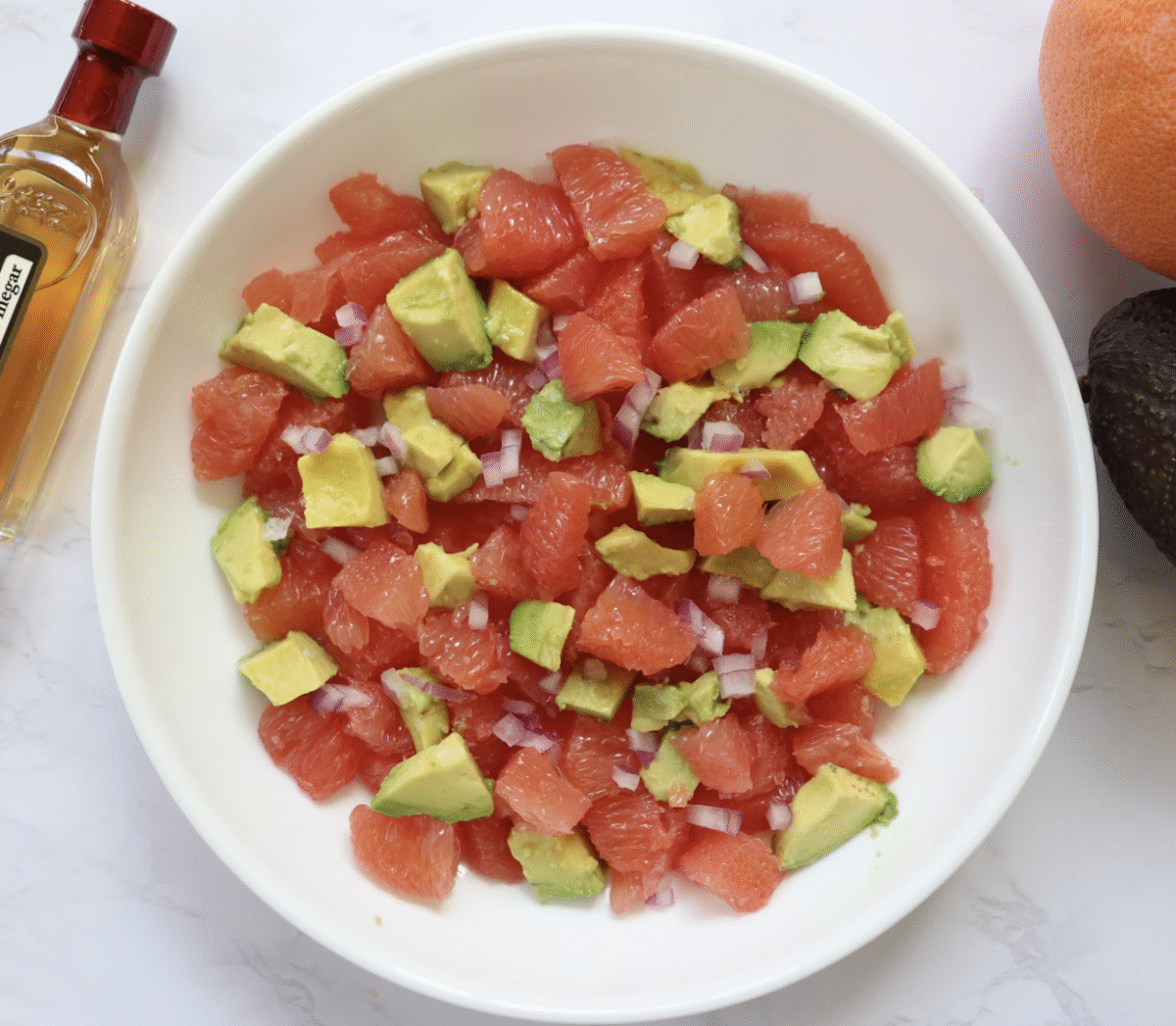 A salad made with grapefruit, avocado and red onion in a white ceramic bowl on a marble countertop.