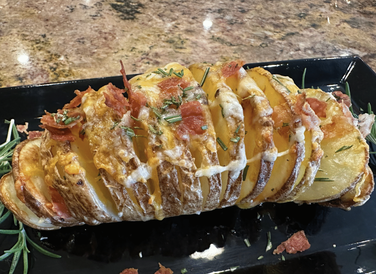 A closeup photo of a cheesy potato topped with rosemary and bacon bits. 