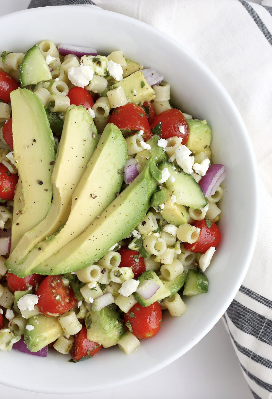 Avocado pasta salad with tomatoes and cucumbers in a white serving bowl. 