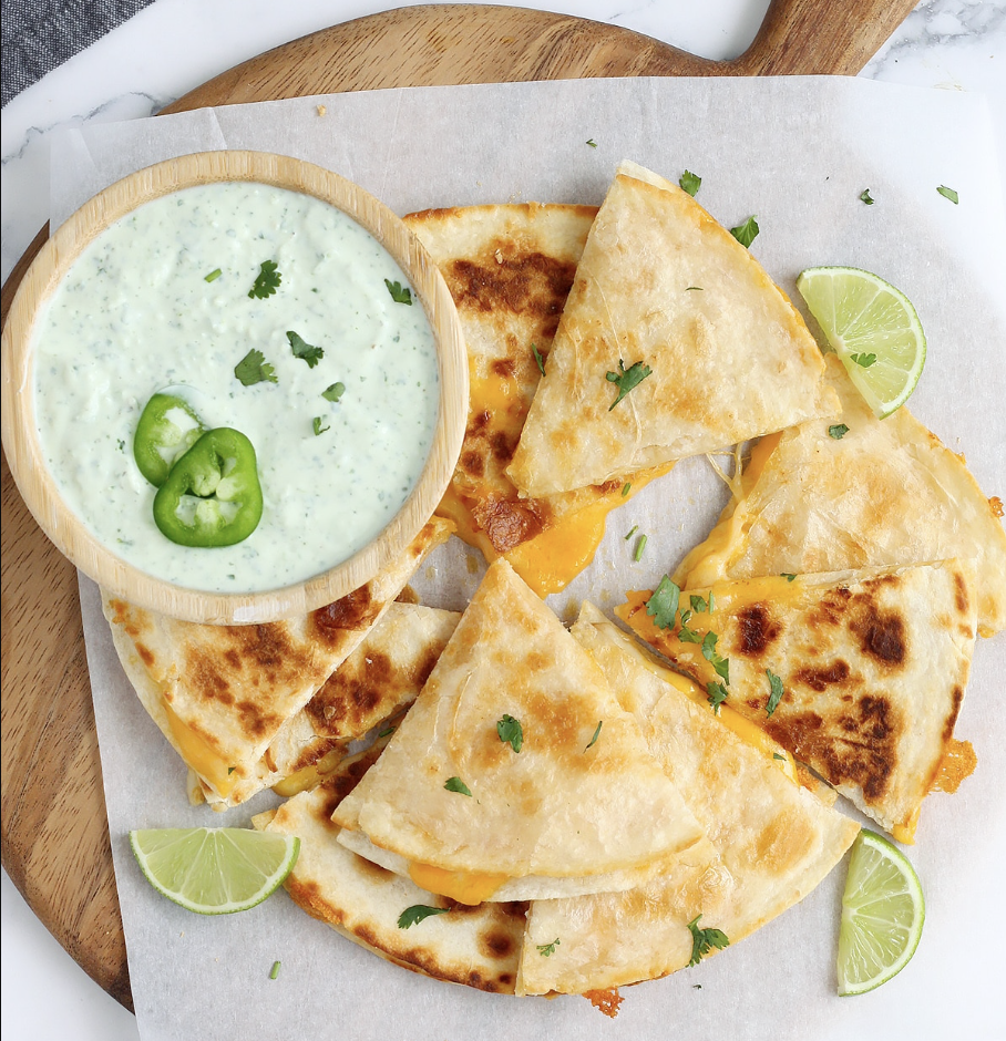 Cheese quesadillas with a creamy dressing on a wooden board with parchment paper. 