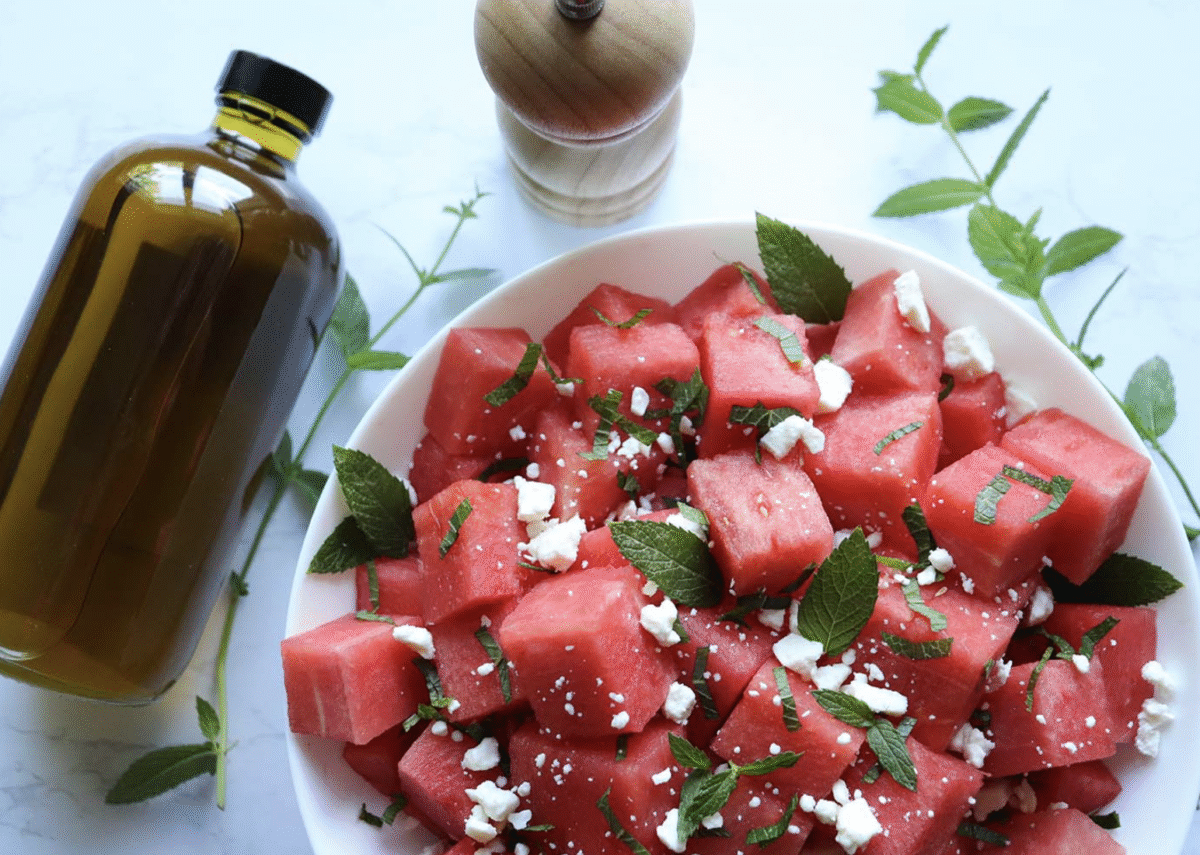 Watermelon mint salad with feta in a serving bowl next to a bottle of olive oil and a pepper grinder.