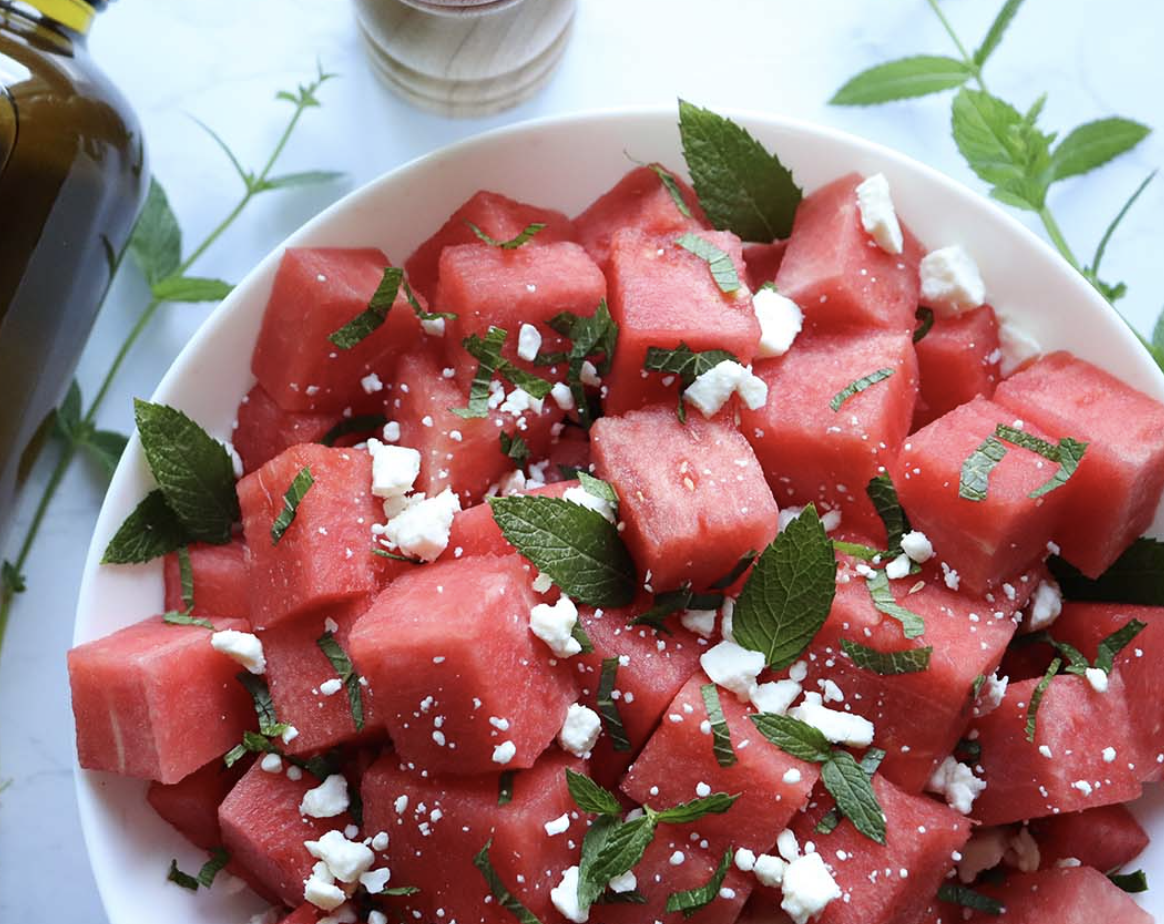 Diced watermelon topped with fresh mint and feta cheese in a serving bowl. 