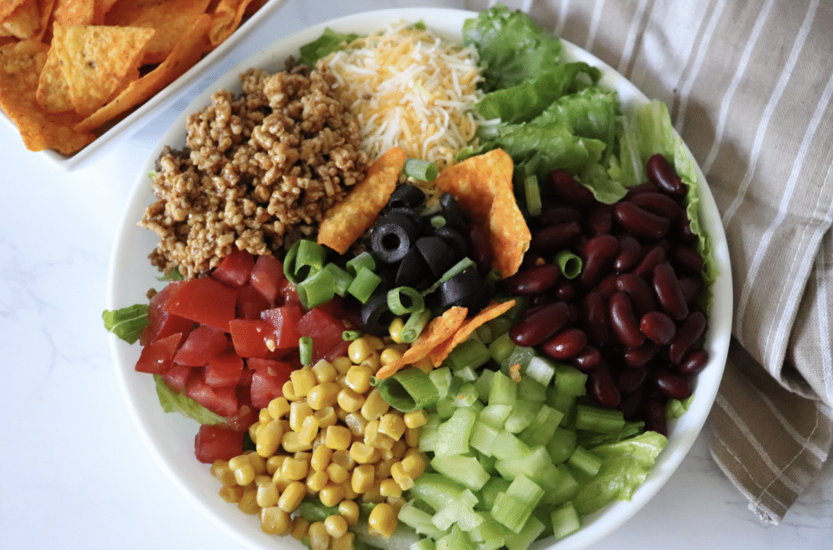 Southwest summer salad in a large white serving bowl topped with corn chips with a striped linen. 