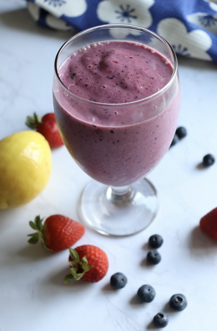A glass of lemon berry power smoothie on a white countertop with fresh berries spread around.