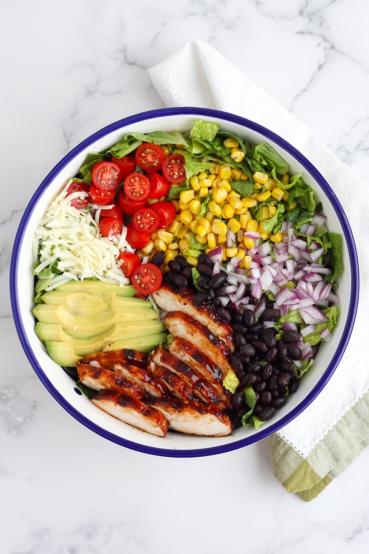 An overhead shot of salad topped with corn, cherry tomatoes, red onion, avocado, and grilled bbq chicken. 