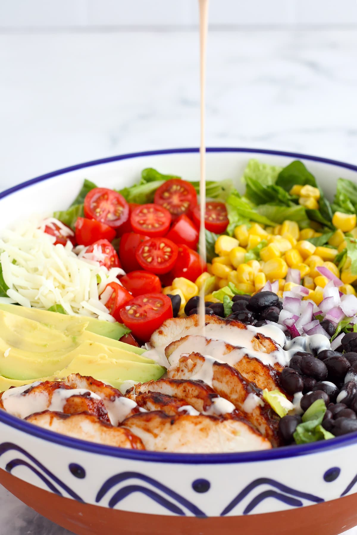 BBQ Chicken Salad drizzled with ranch dressing in a large white serving bowl. 