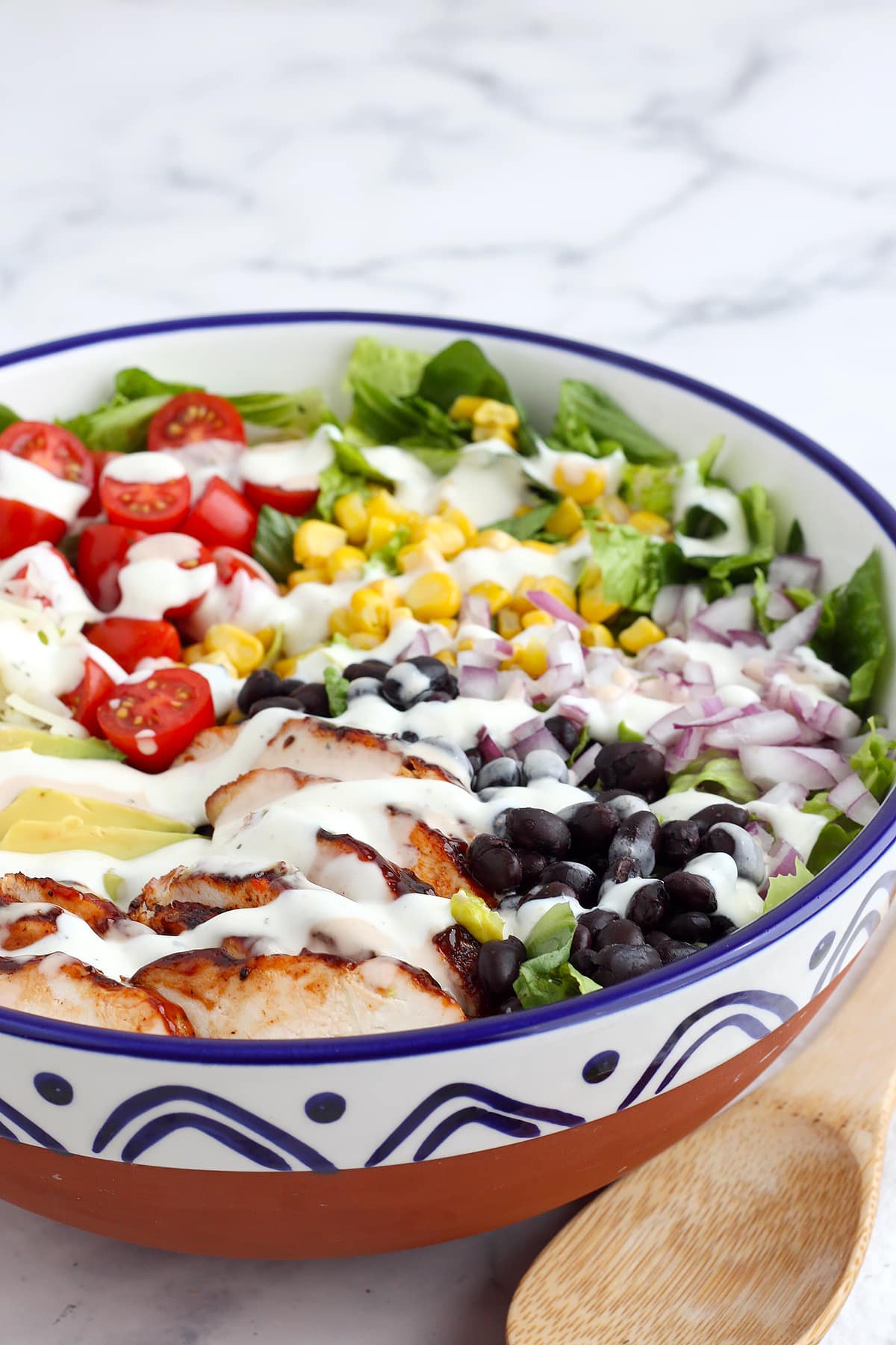 BBQ Chicken Salad in a ceramic serving bowl with black beans, corn and tomatoes and drizzled with ranch dressing. 