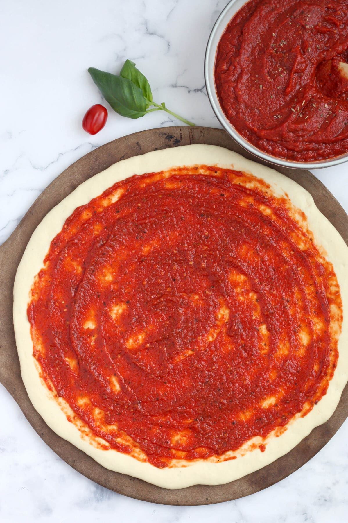 Pizza dough on a pizza stone spread with thick and delicious homemade pizza sauce. 