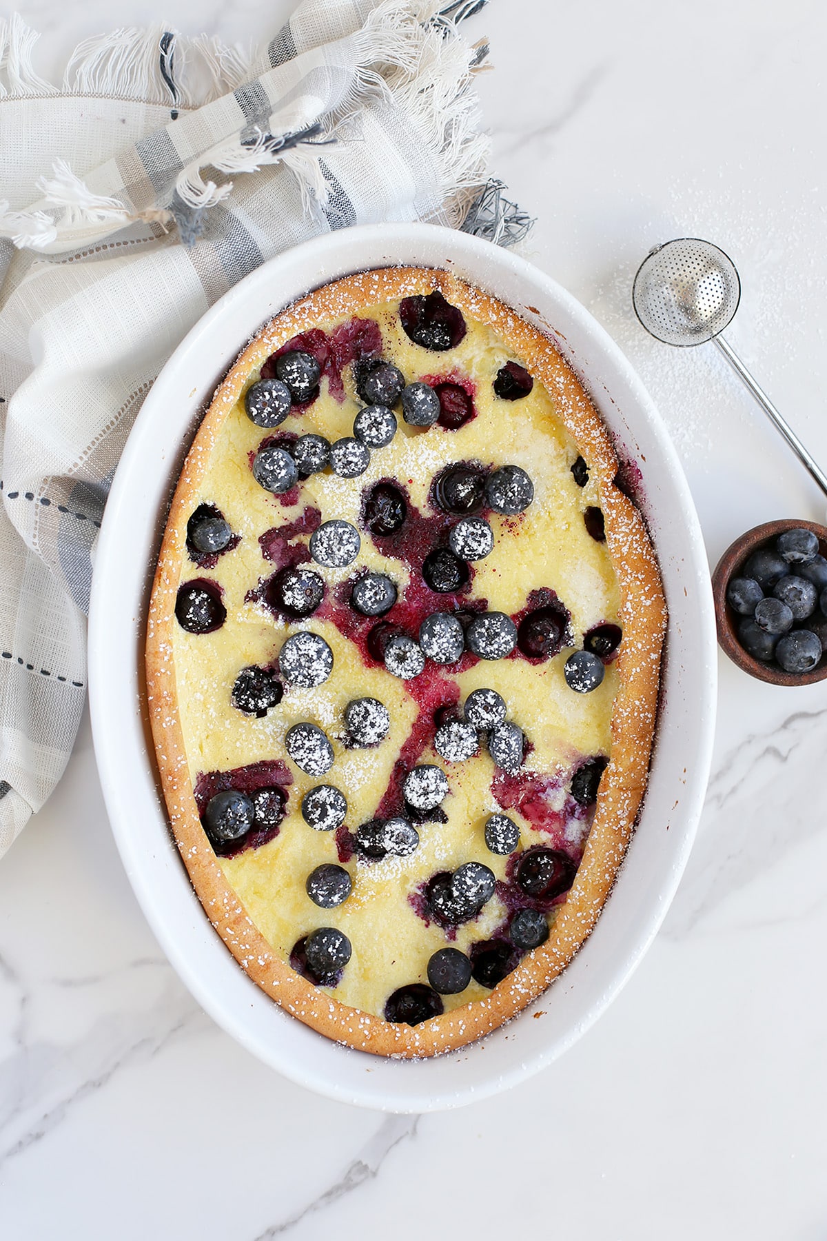 Blueberry pancake baked into a casserole dish with a striped linen in the background. 