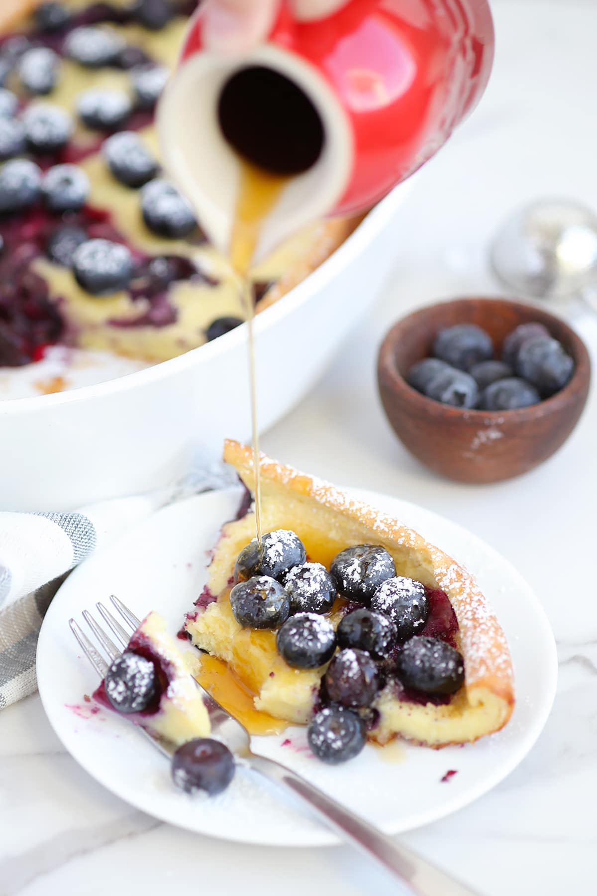 Dutch baby pancake with blueberries and drizzled with maple syrup on a white plate. 