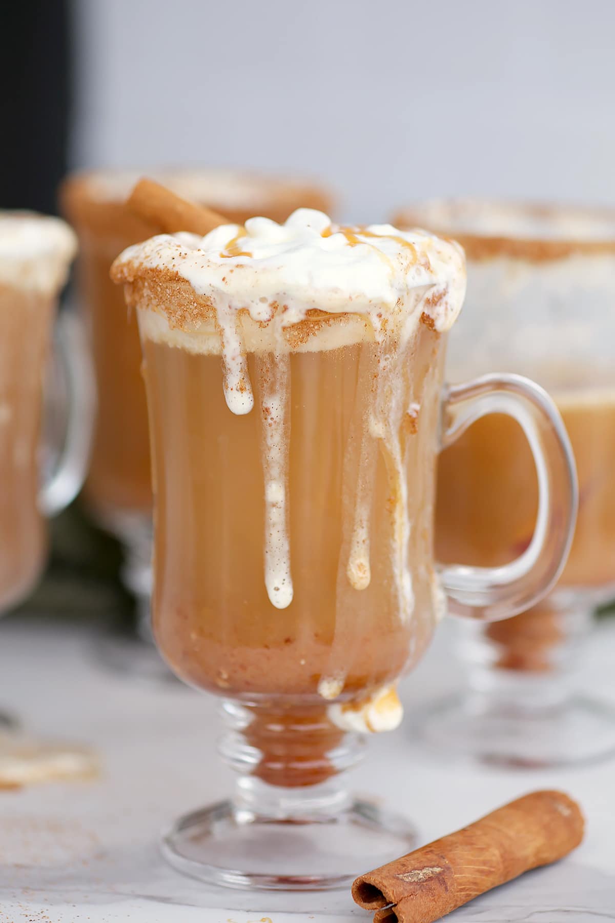 A mug of cider with whipped cream dripping down the sides. 