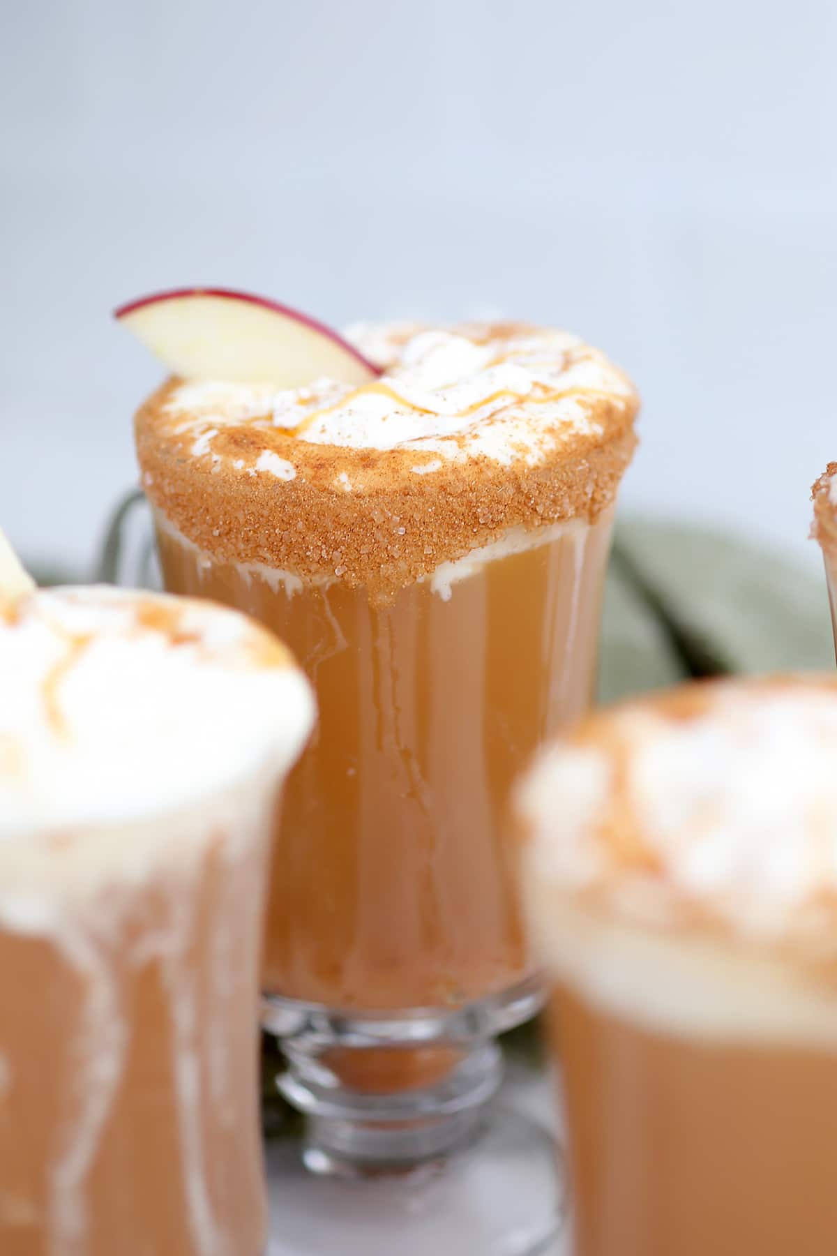 A mug dipped in cinnamon sugar and filled with apple cider, topped with whipped cream, caramel, and an apple slice. 