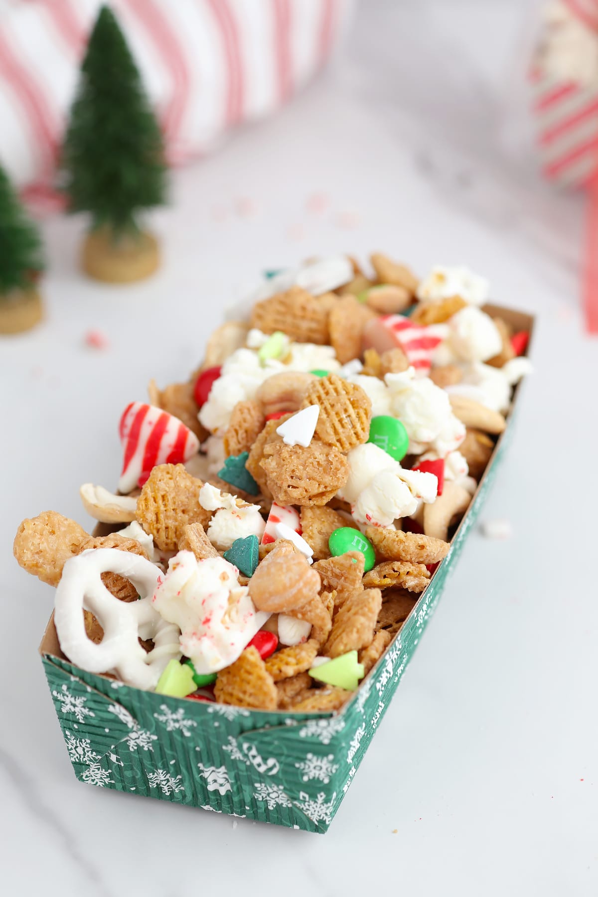 Christmas snack mix made with cereal, nuts, popcorn, and Christmas candies in a gifting container. 