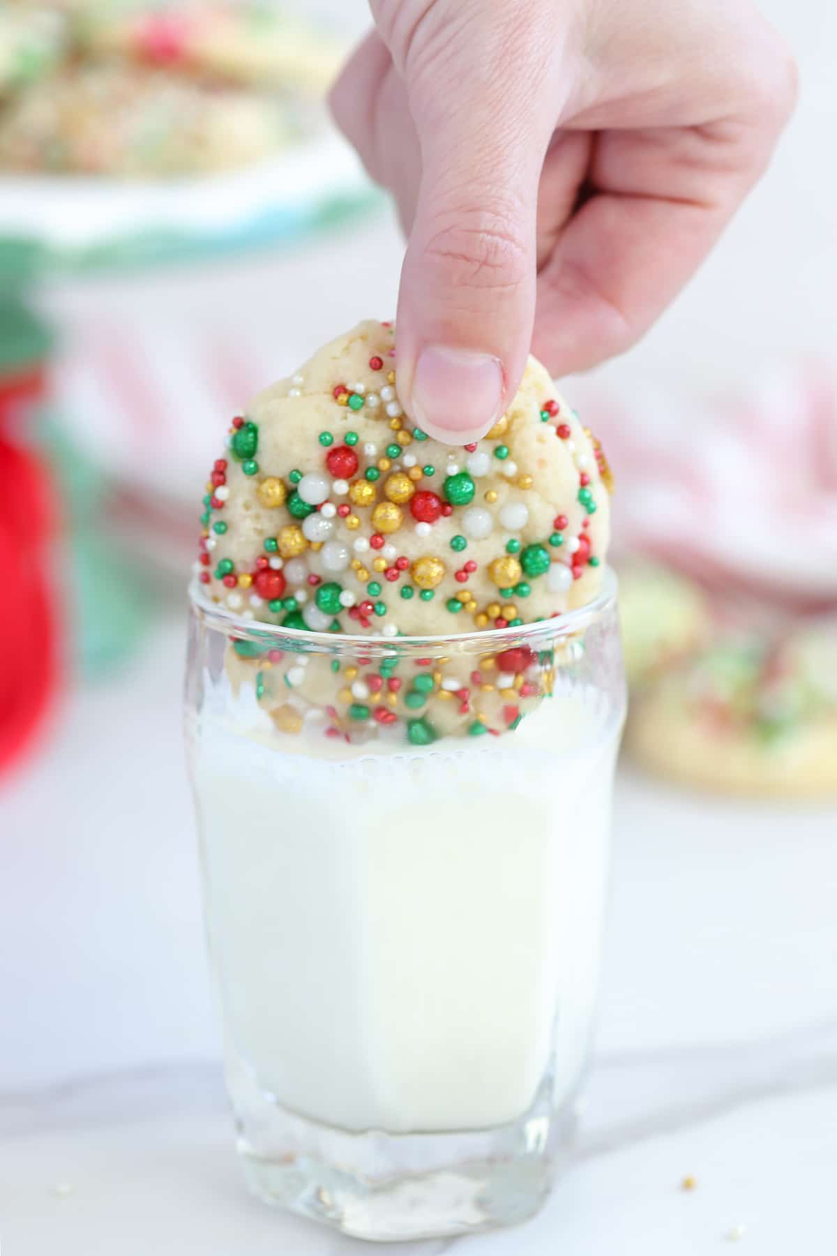A hand dipping a sugar cookie into a glass of milk. 