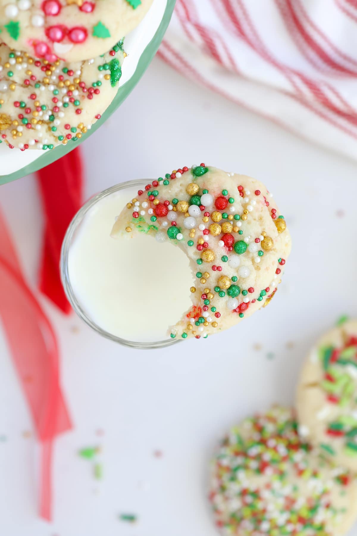 A Christmas sugar cookie with a bite taken out resting on the rim of a glass of milk. 