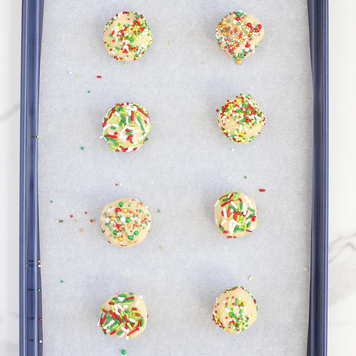 Balls of sugar cookie dough rolled in sprinkles on a baking sheet. 