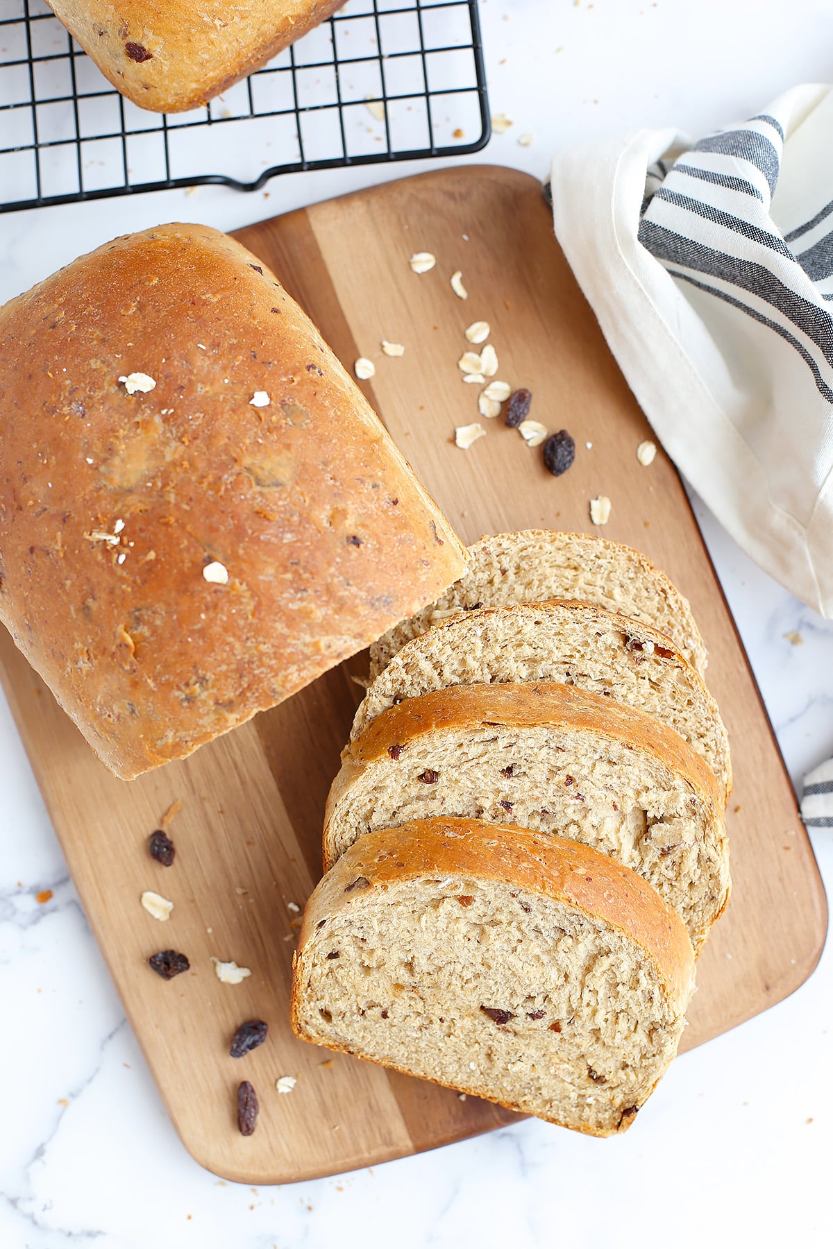 An overhead shot of a sliced loaf of cinnamon raisin bread on a wooden cutting board with a striped linen. 