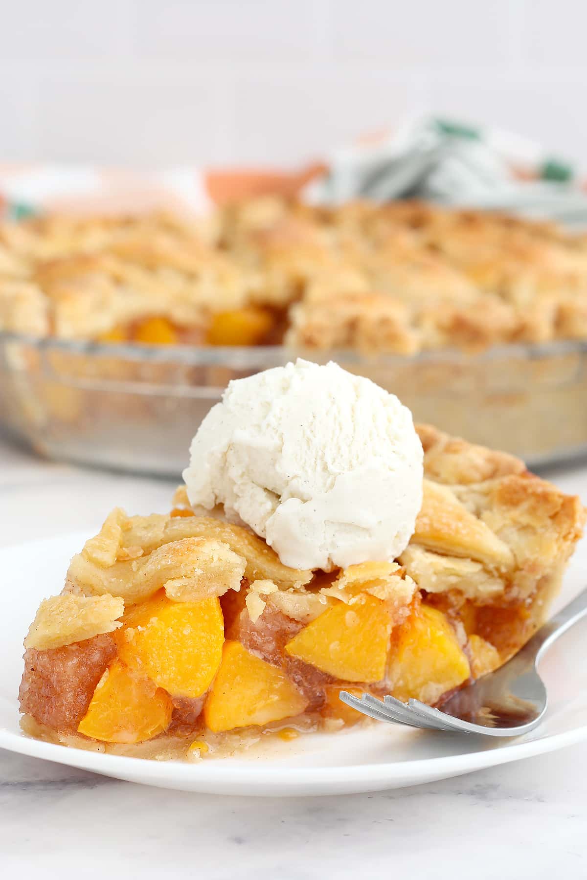 A slice of peach pie on a serving plate topped with vanilla ice cream. 