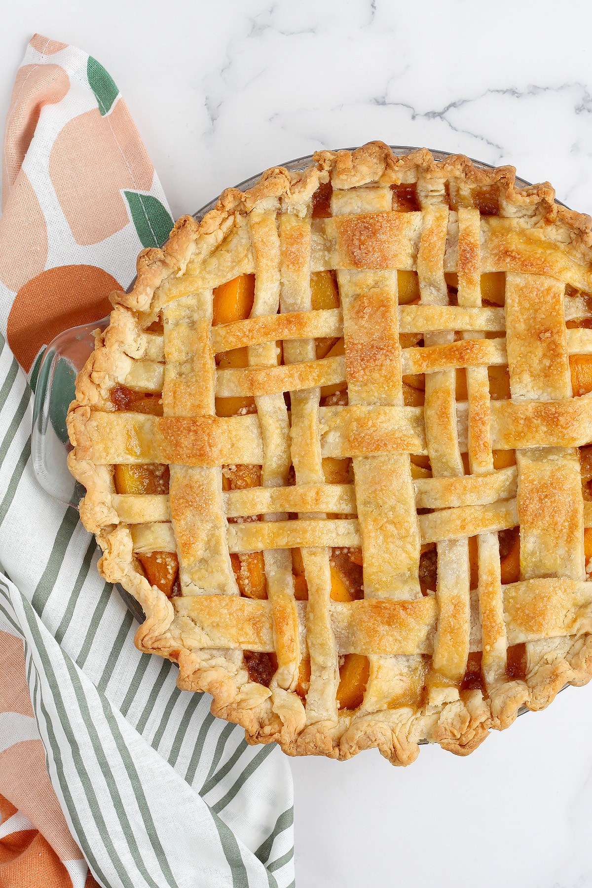 Classic peach pie with a weaved crust in a glass pie plate. 