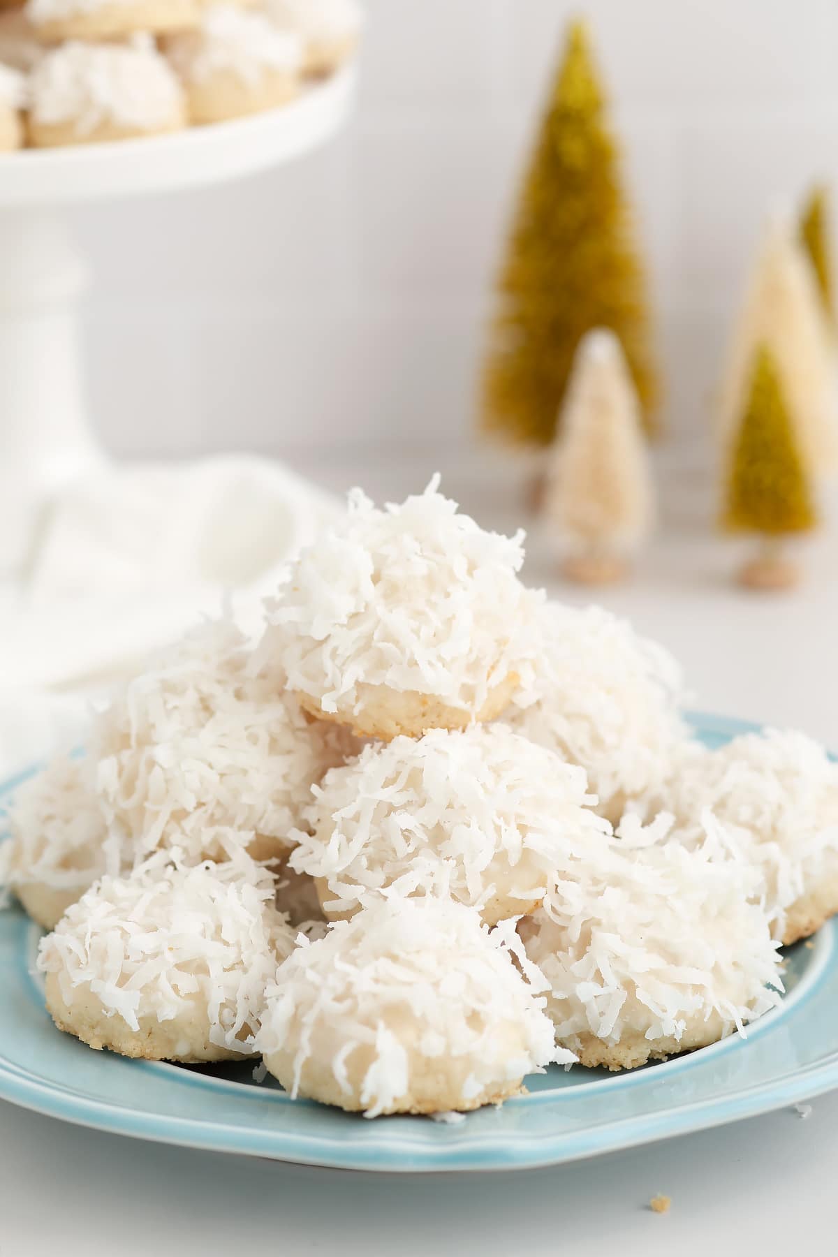 Coconut Snowball cookies topped with shredded coconut and piled on a blue serving plate. 
