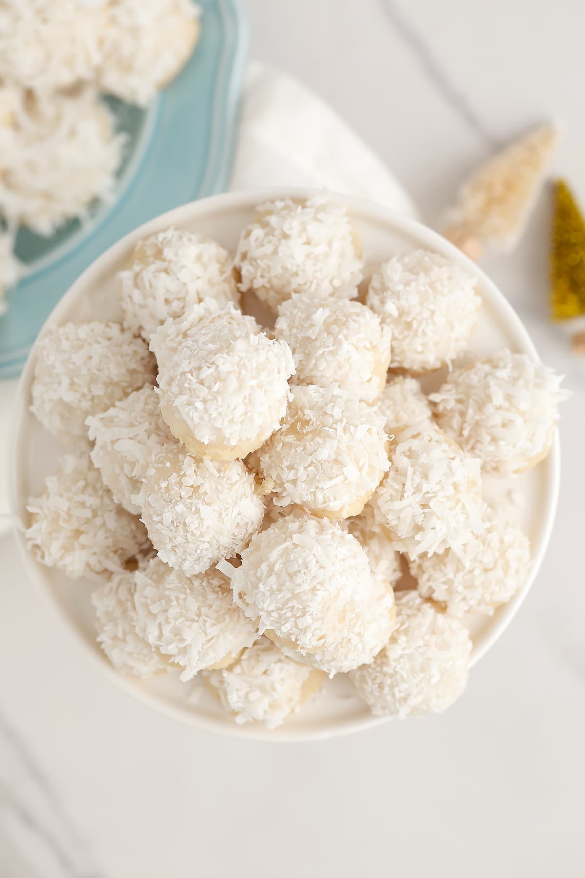 Coconut snowball cookies stacked on a white serving platter. 