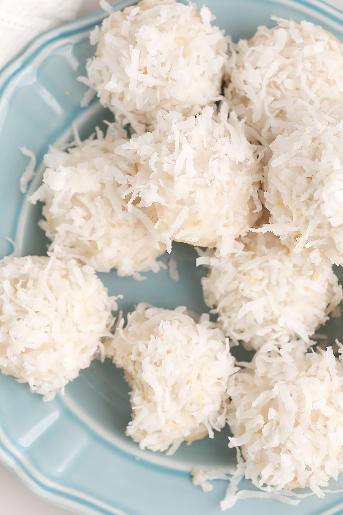 Homemade cookies dipped in icing and coated with flaked coconut on a blue plate. 