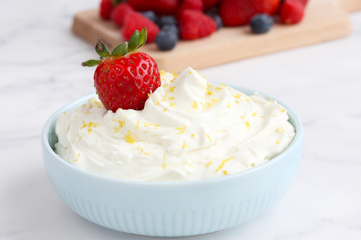 fluffy lemon fruit dip with a fresh strawberry in a small blue bowl.
