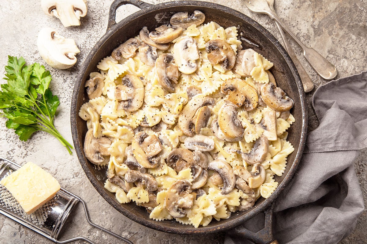 creamy mushroom pasta in a cast iron skillet with parmesan cheese, parsley and mushrooms in the background. 