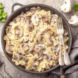 creamy mushroom pasta in a cast iron skillet with parmesan cheese, parsley and mushrooms in the background.