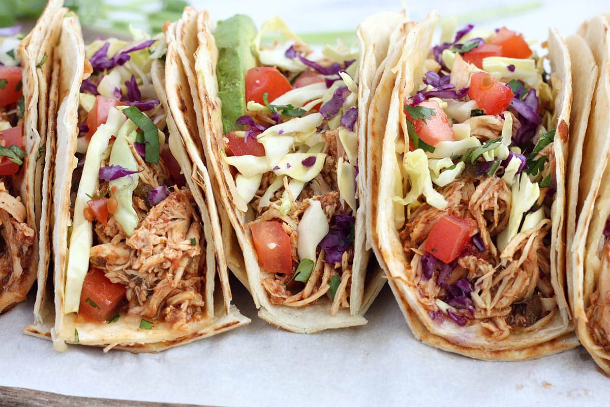 sideview of chicken tacos topped with cabbage, tomatoes and avovcado