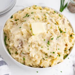 crockpot mashed potatoes in a white bowl with chives and butter on top, blue and white napkin in the background