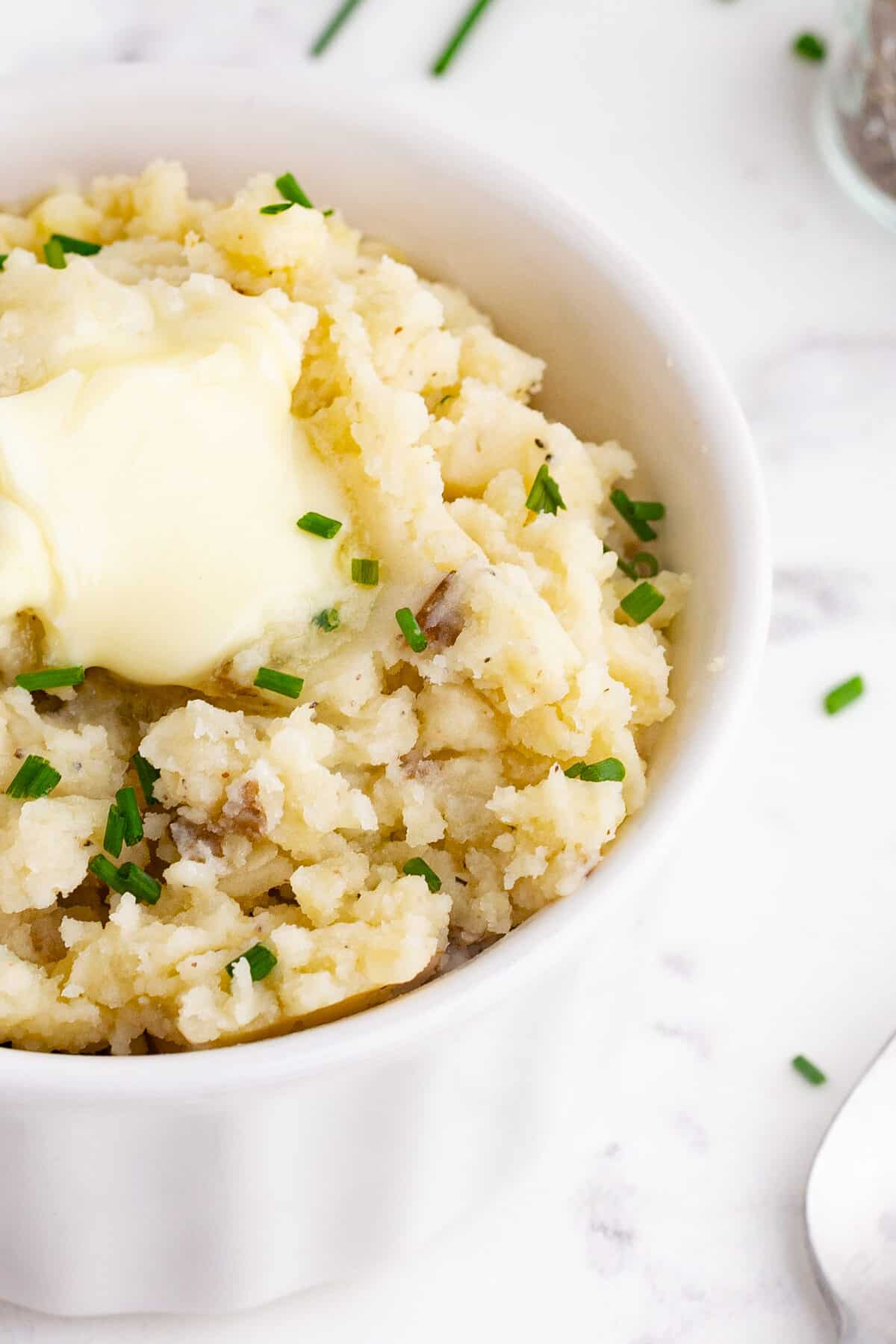 closeup of a bowl of mashed potatoes with chives, potatoes skins, and butter on top