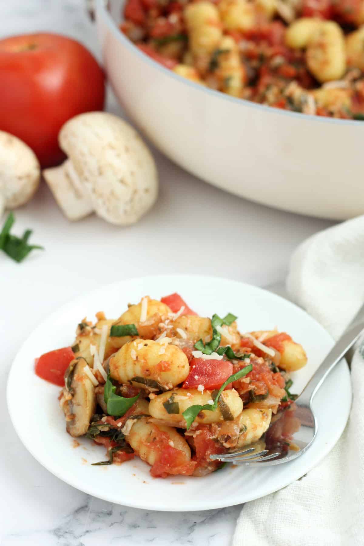 a serving of easy gnocchi on a white plate with veggies in the background