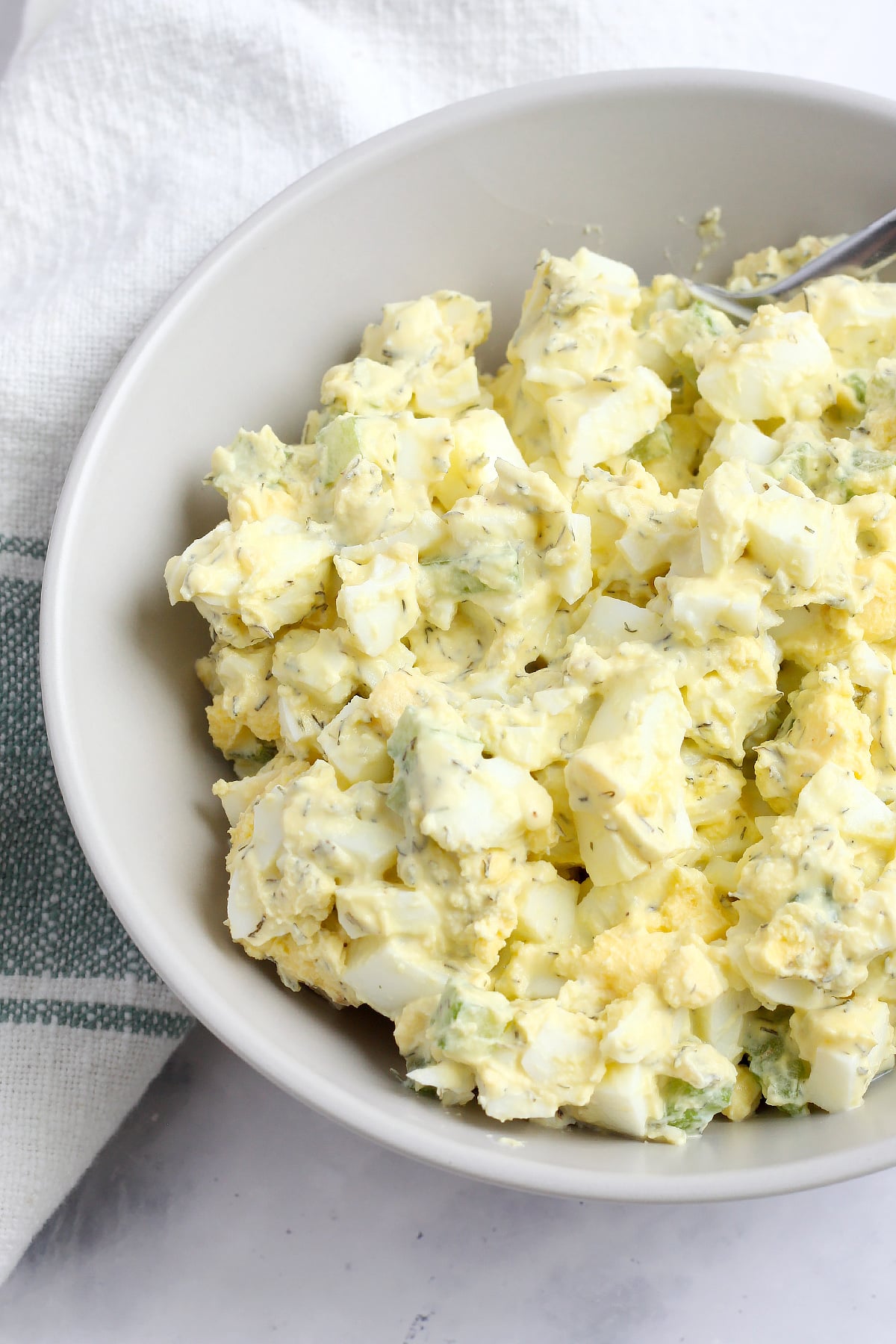 Egg salad in a taupe colored serving bowl with a white linen. 