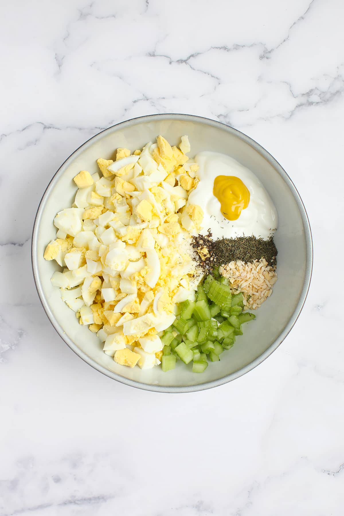 A mixing bowl with all of the ingredients for homemade egg salad. 