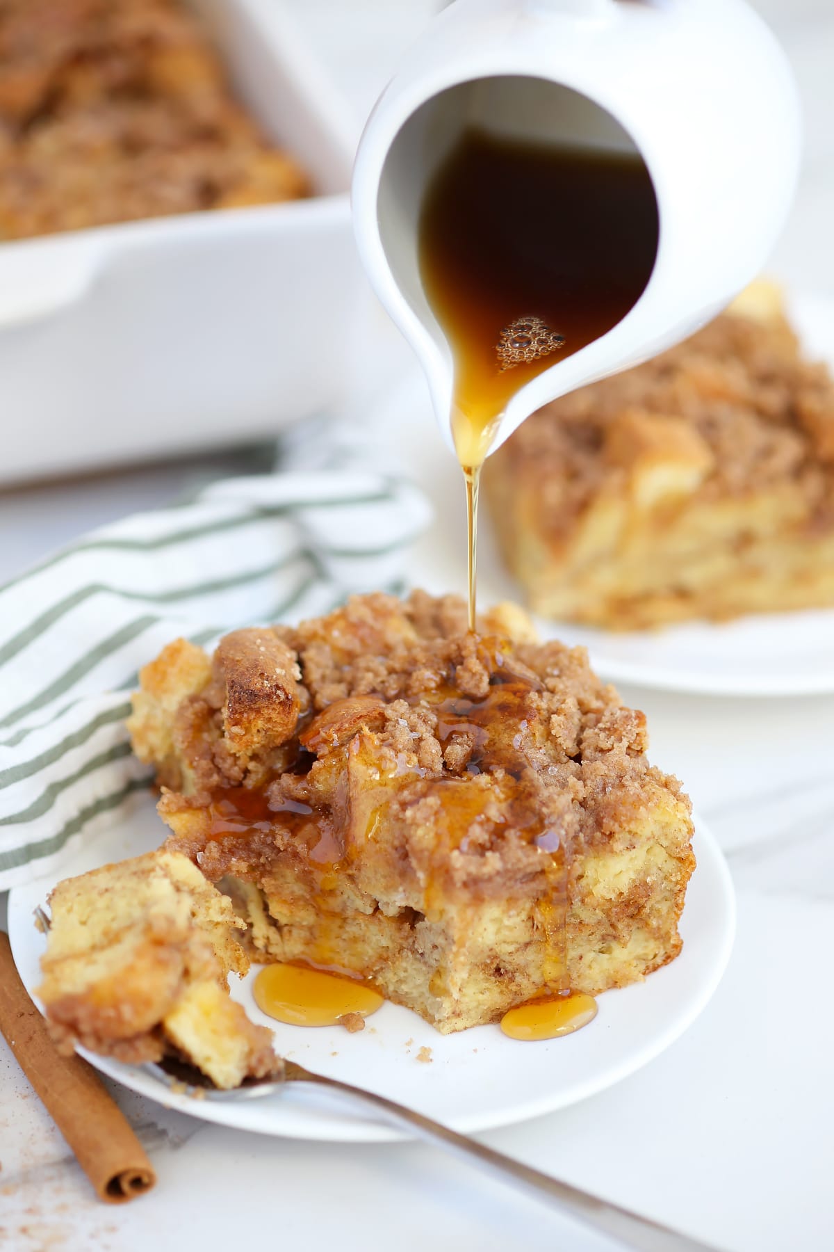 A serving of french toast casserole on a white plate being drizzled with maple syrup. 