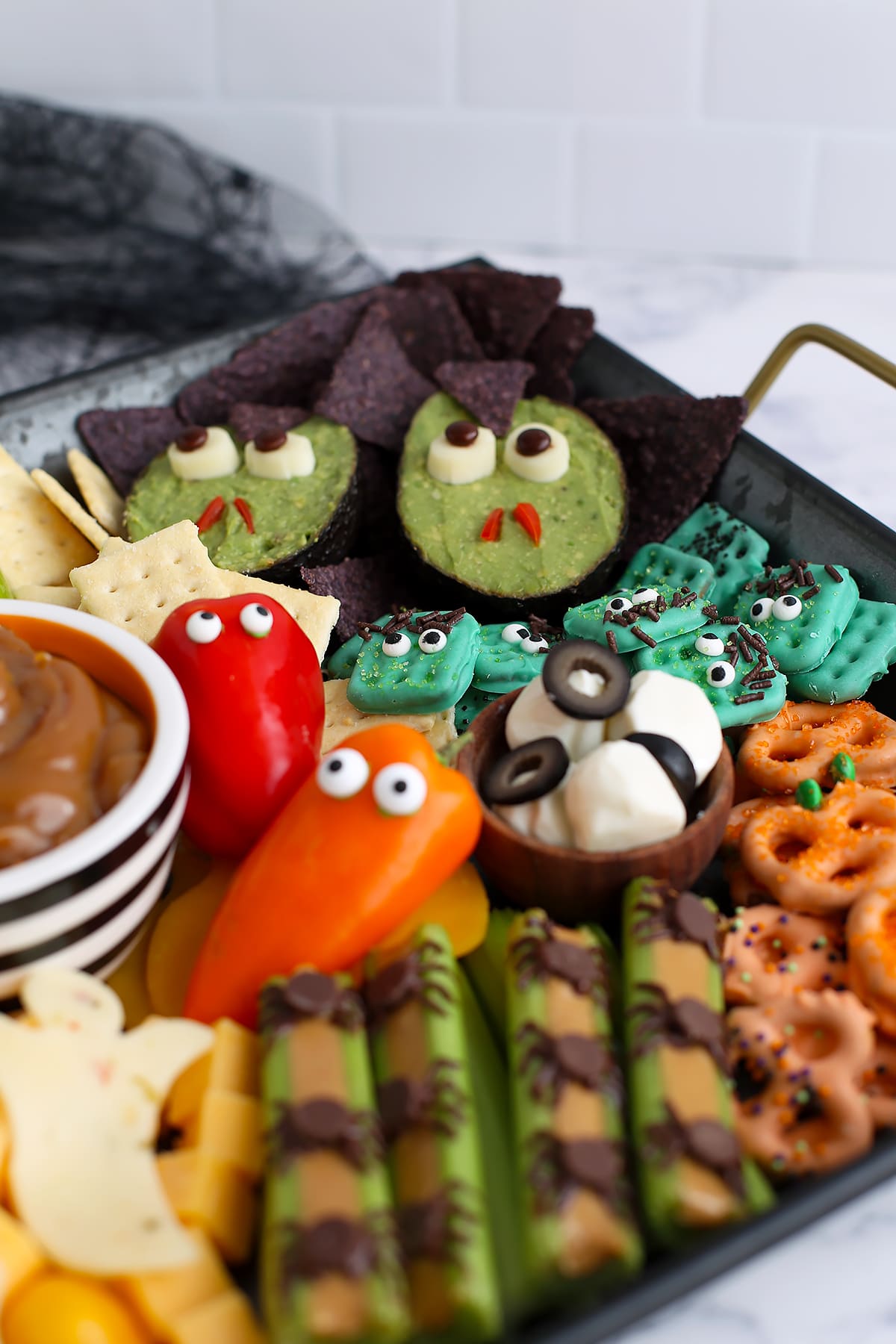 A close up image of halloween snacks on a charcuterie board with peppers, cheese, pretzels, and avocados. 