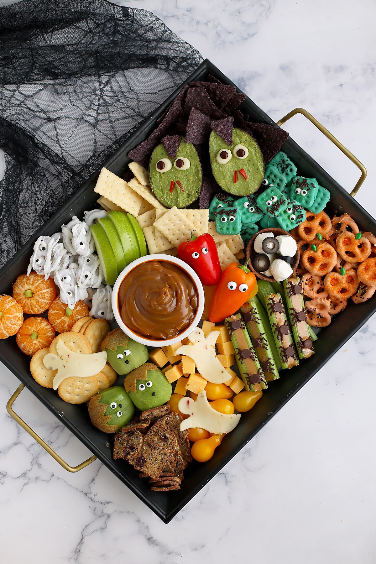 A black serving tray topped with assorted halloween snack foods with a black spider web linen in the background. 