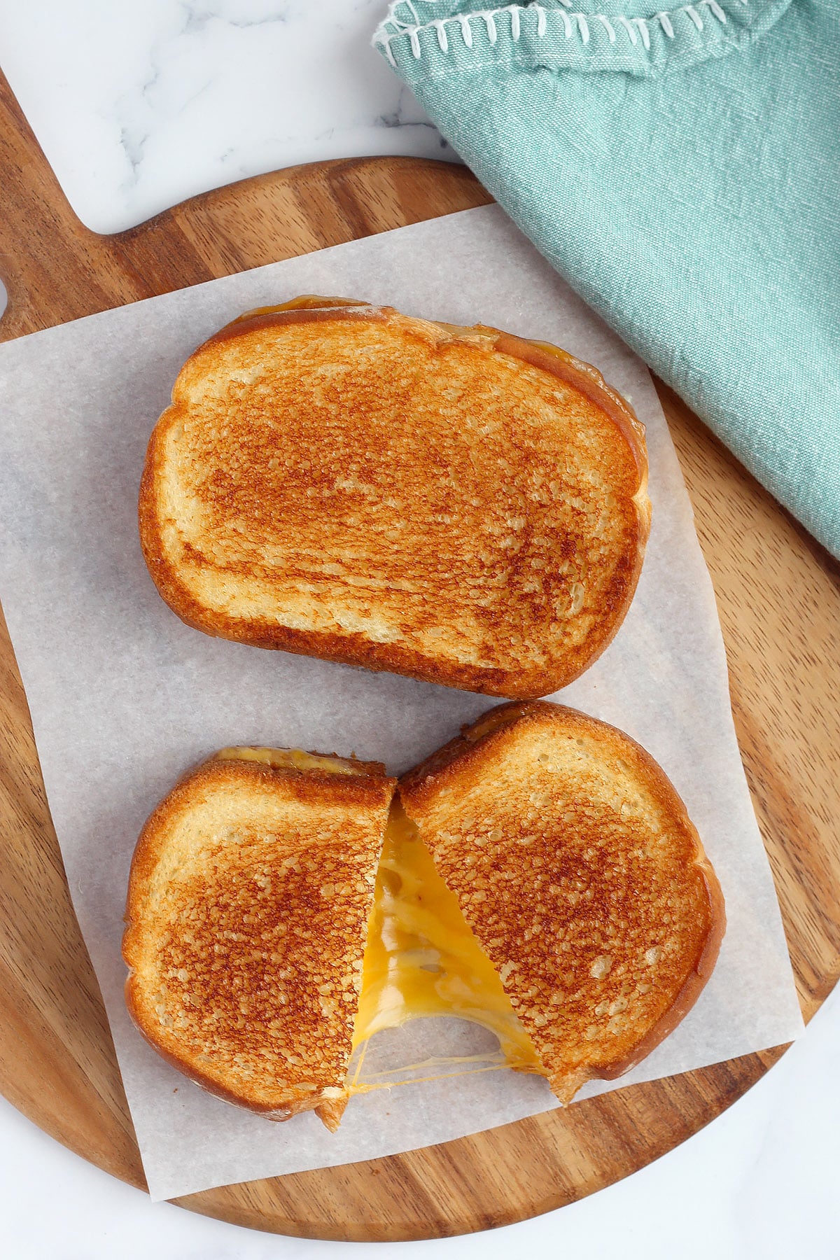 Grilled cheese sandwiches on parchment covered cutting board with a green linen. 