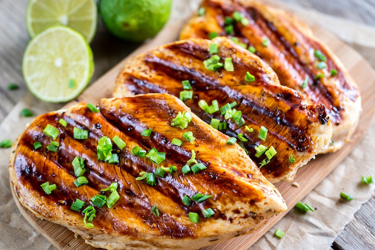 grilled chicken breasts with coconut and lime marinade on a wooden cutting board with fresh limes in the background