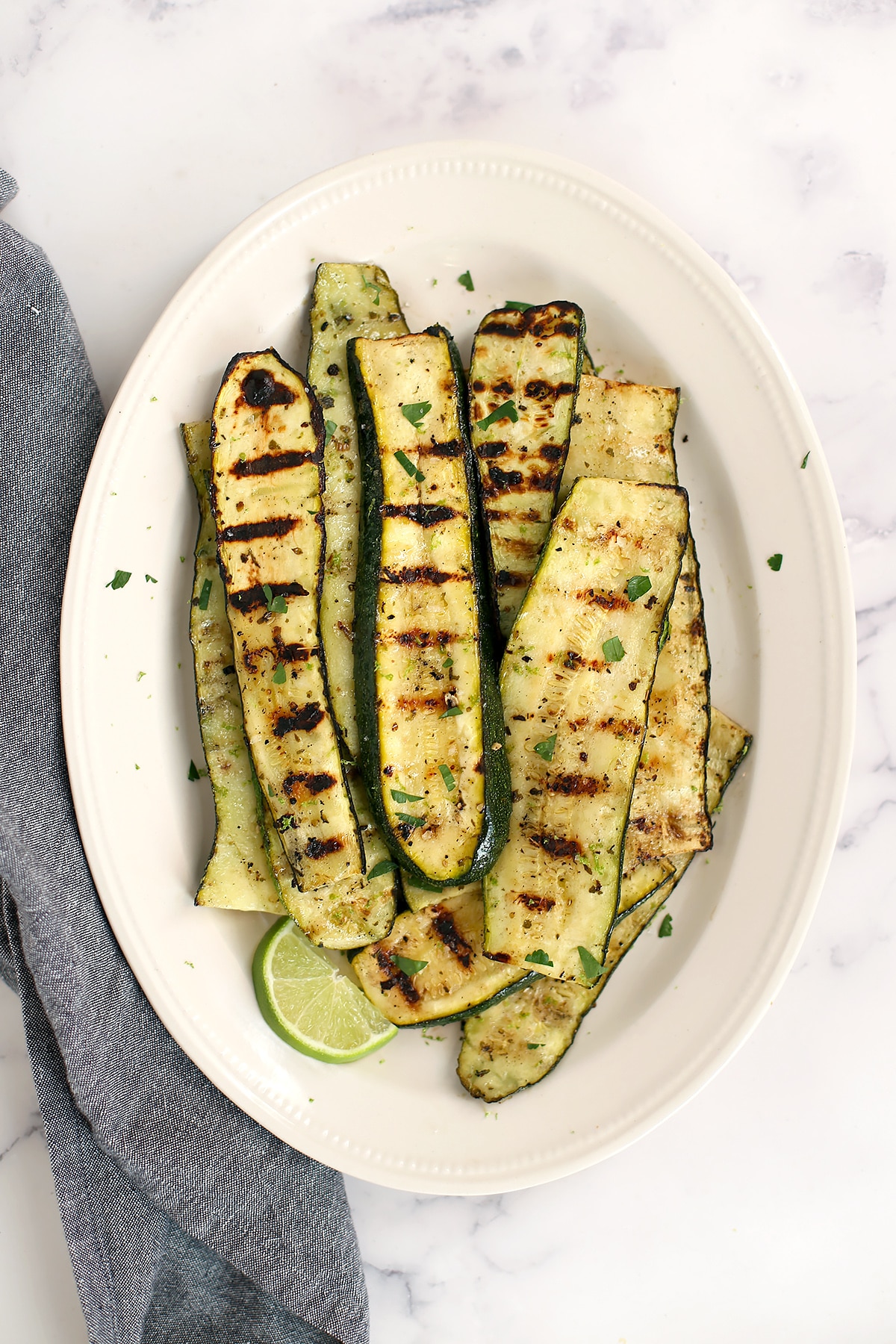 Grilled zucchini on a white serving platter with lime wedges. 