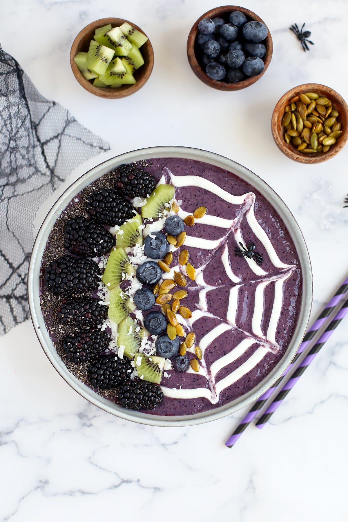 A bowl filled with a blueberry smoothie and topped with a spooky design and fresh fruit. 