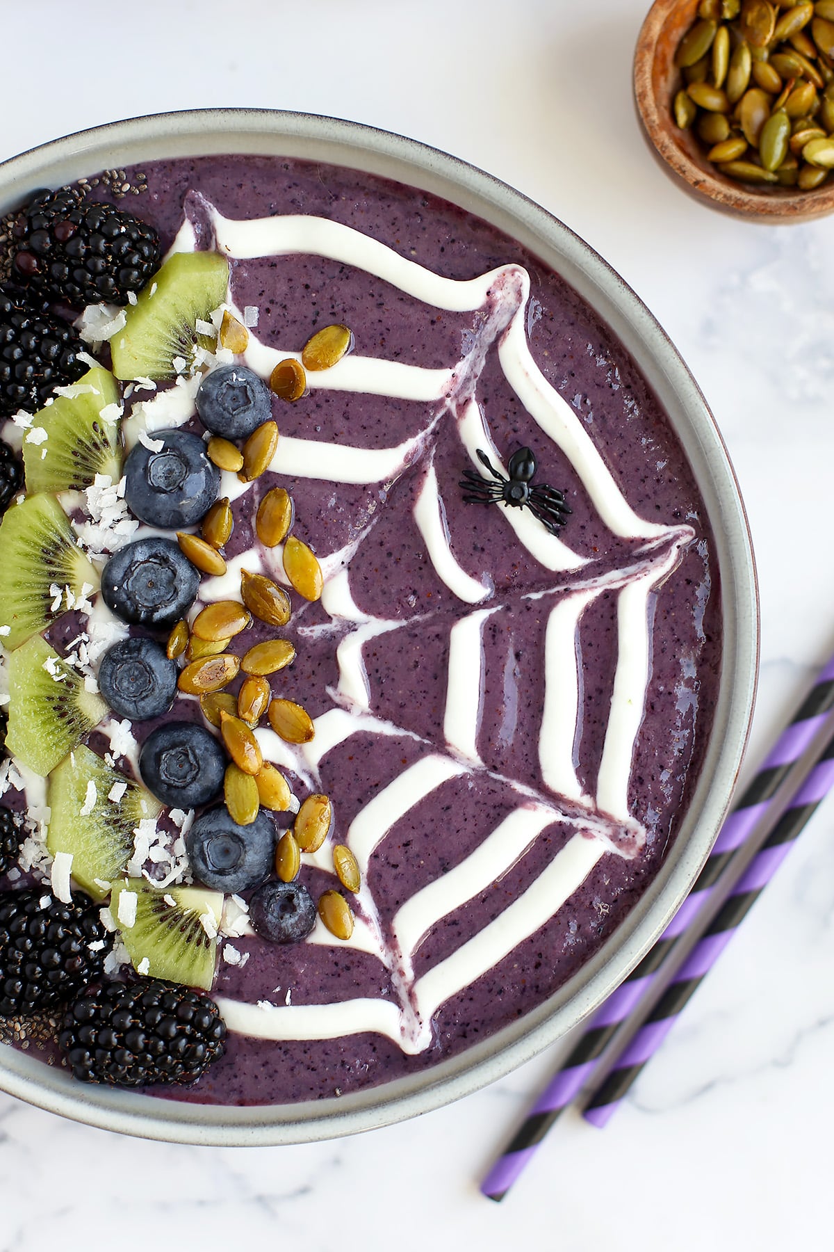 A blueberry smoothie bowl topped with a greek yogurt web design, fresh blueberries, kiwi, and pumpkin seeds. 