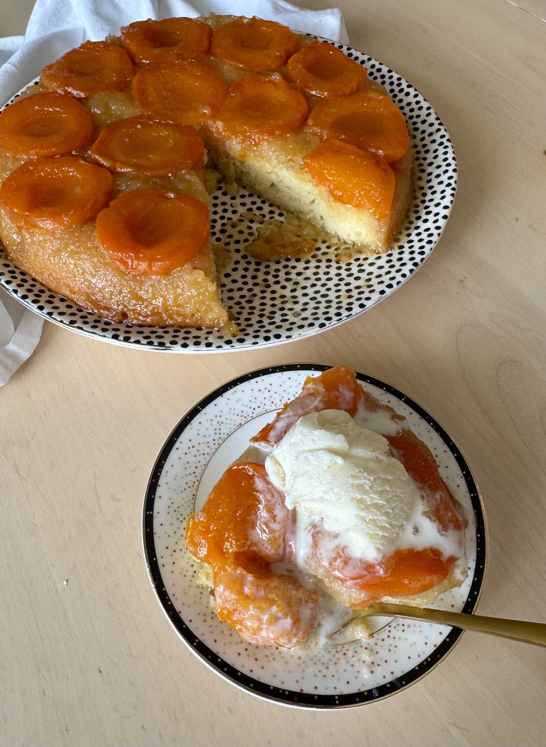 A caramelized apricot tart on a black and white serving plate with a scoop of vanilla ice cream melting on top.