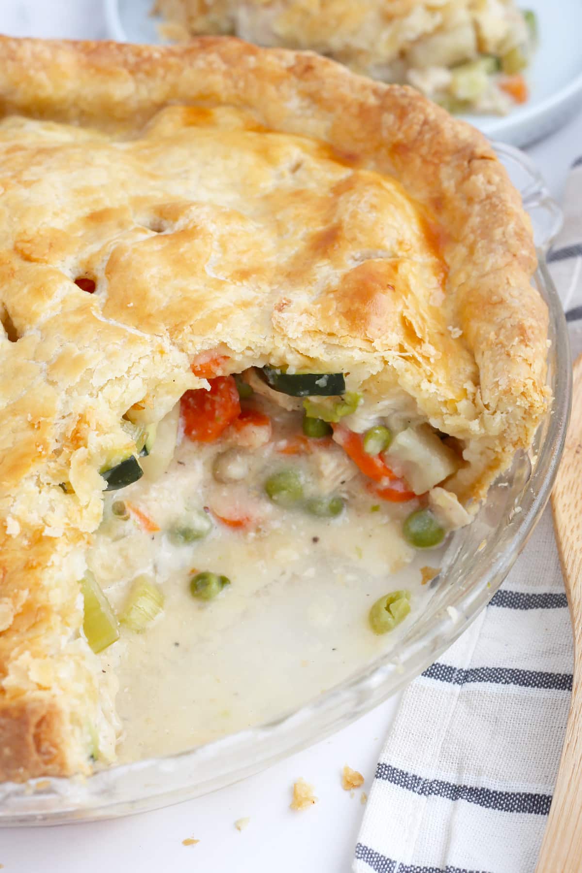 Chicken Pot Pie in a glass dish that has been scooped out to show all the chicken and vegetables in a creamy sauce. 