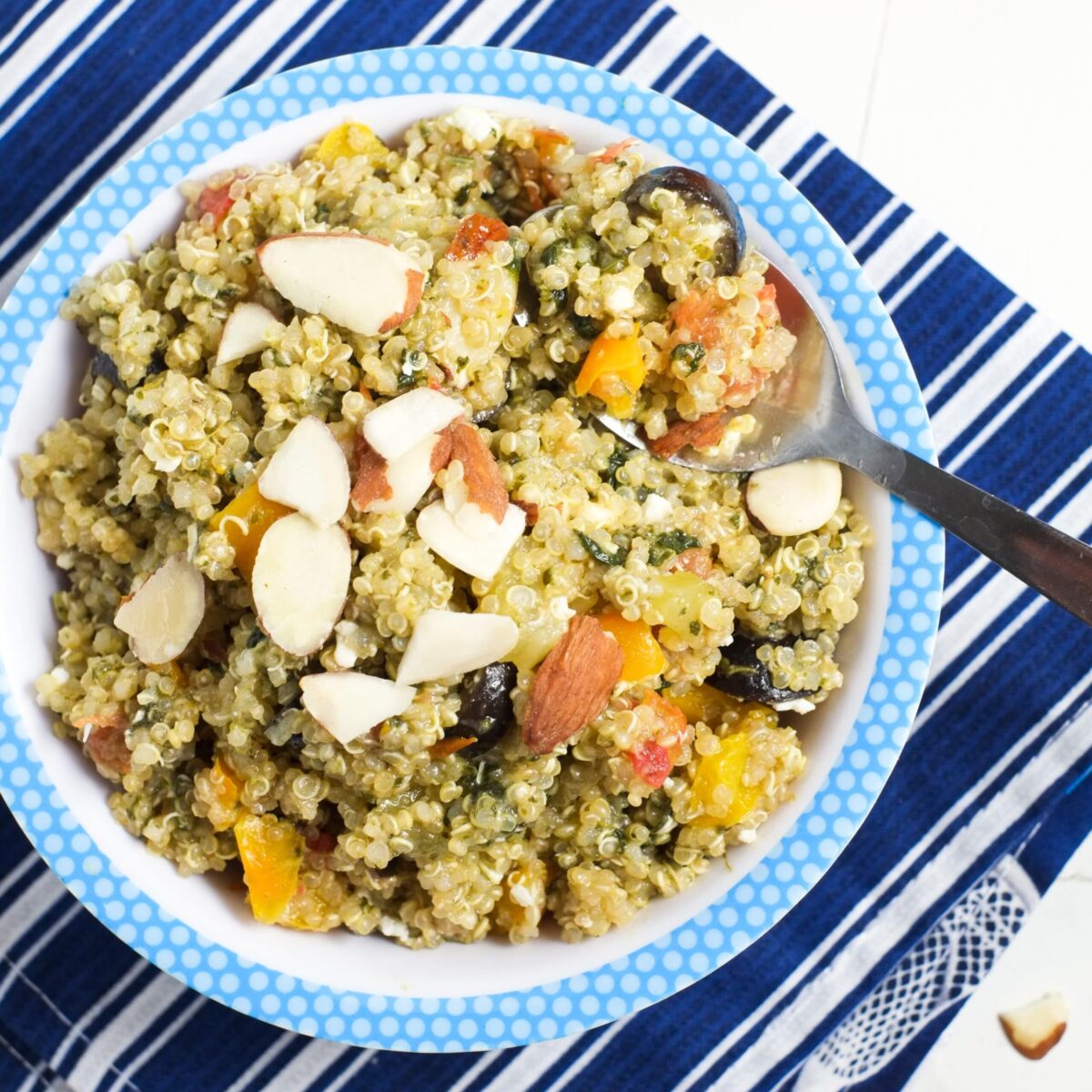 A bowl of quinoa and veggies in a bowl over a striped blue napkin with a spoon. 
