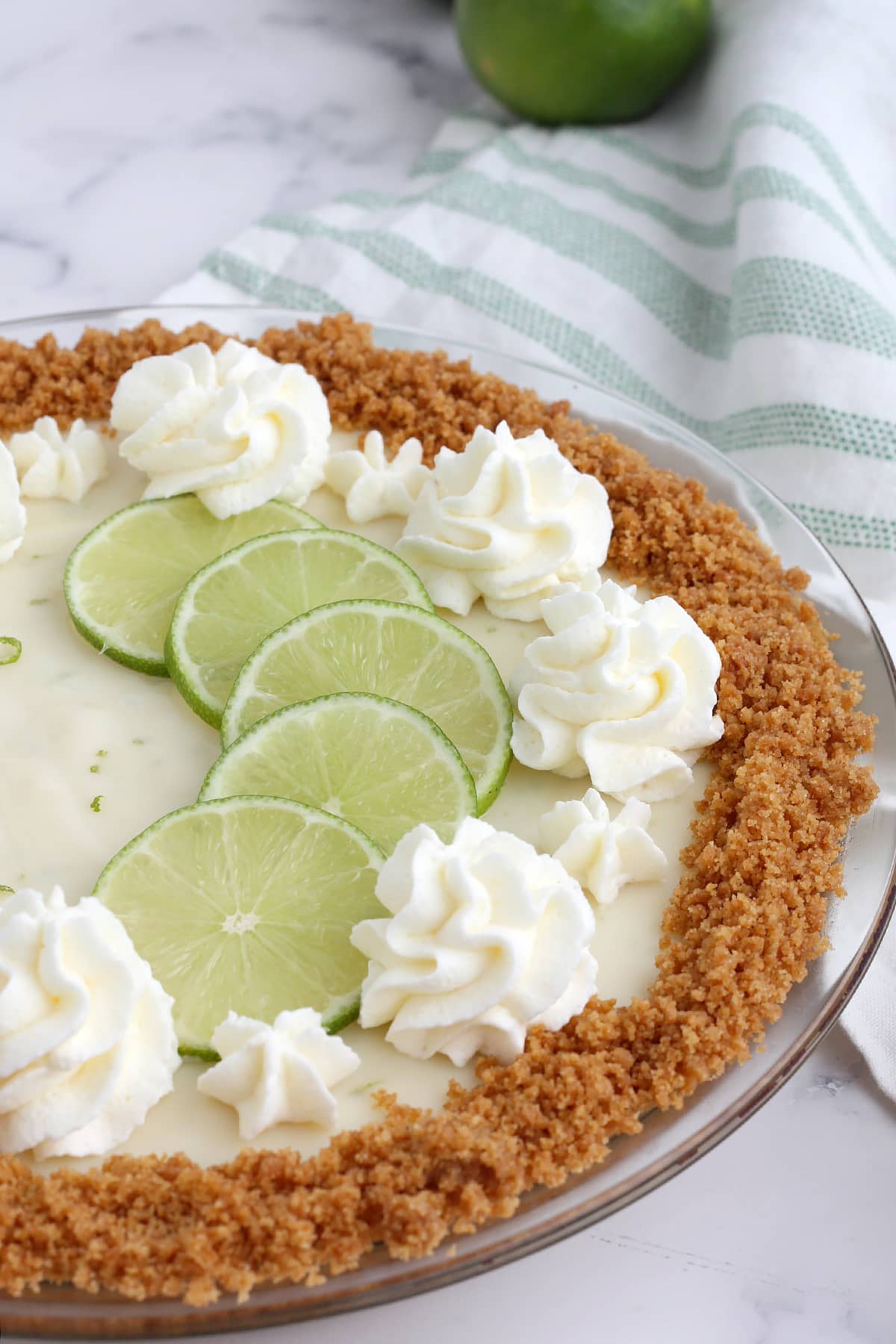 A close up picture of key lime pie topped with whipped cream and thinly sliced limes. 